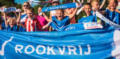 Decoratieve foto van kinderen op een sportveld. De kinderen dragen sportkleding en dragen vlaggen en banners waarop Rookvrije Generatie staat.